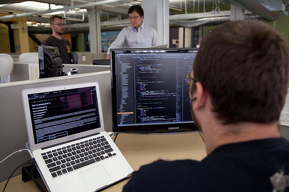 A developer coding at two screens in an office