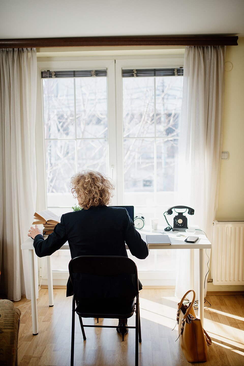 A person working at a desk with a laptop and telephone near a window