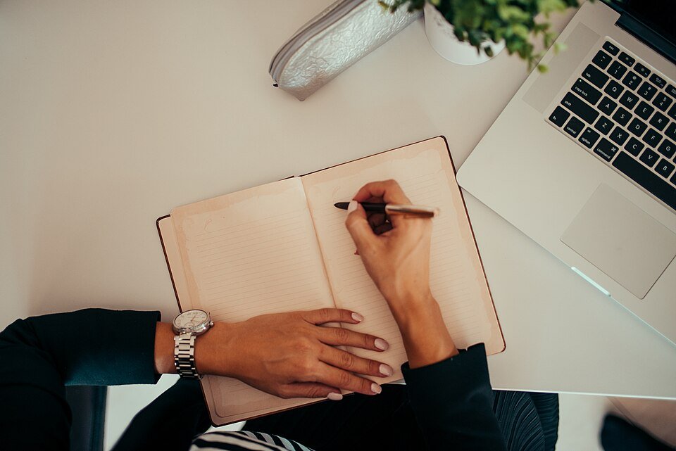 A person writing notes beside a laptop at a modern workspace