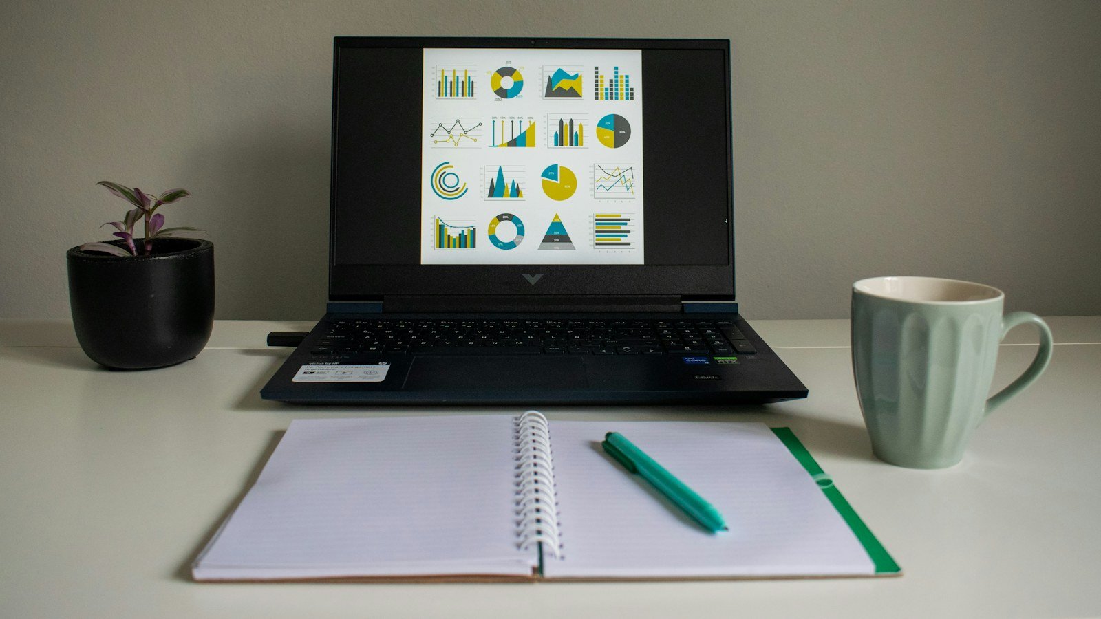 Laptop with charts beside a notebook and coffee mug
